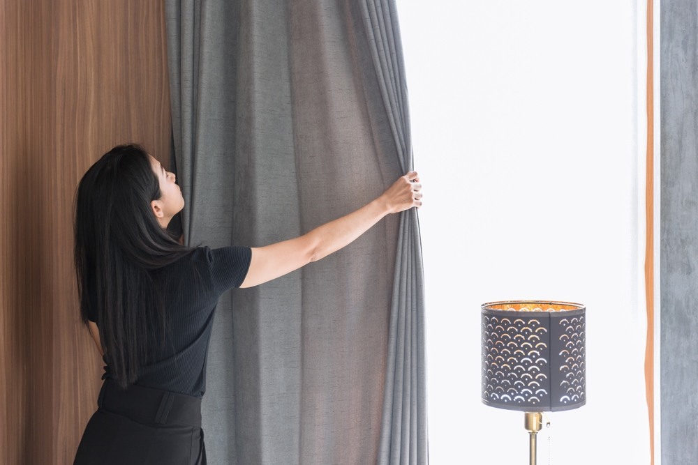 Girl closing curtains of her apartment